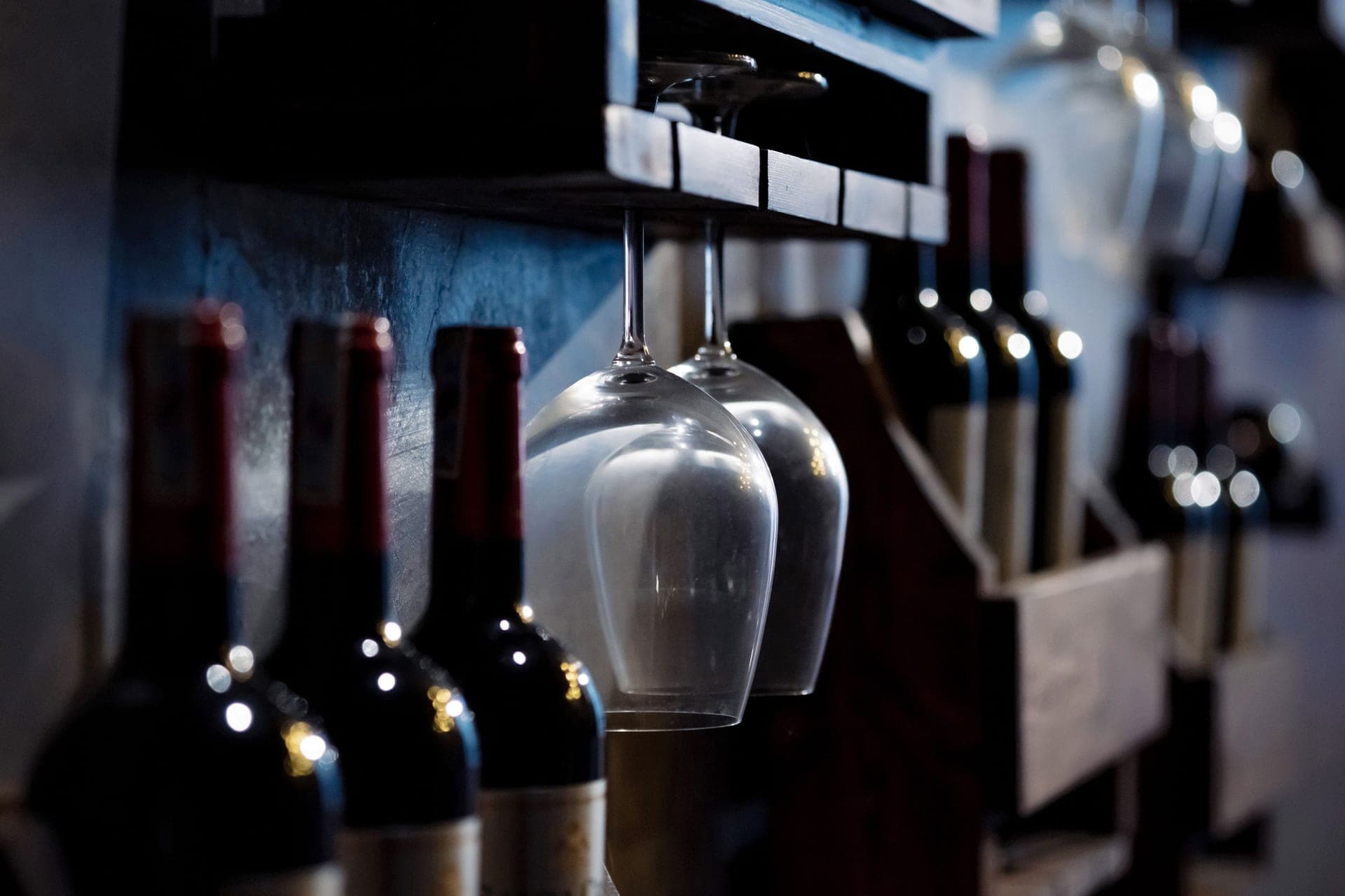 Wine bottles and glasses stored on wooden shelving in low light