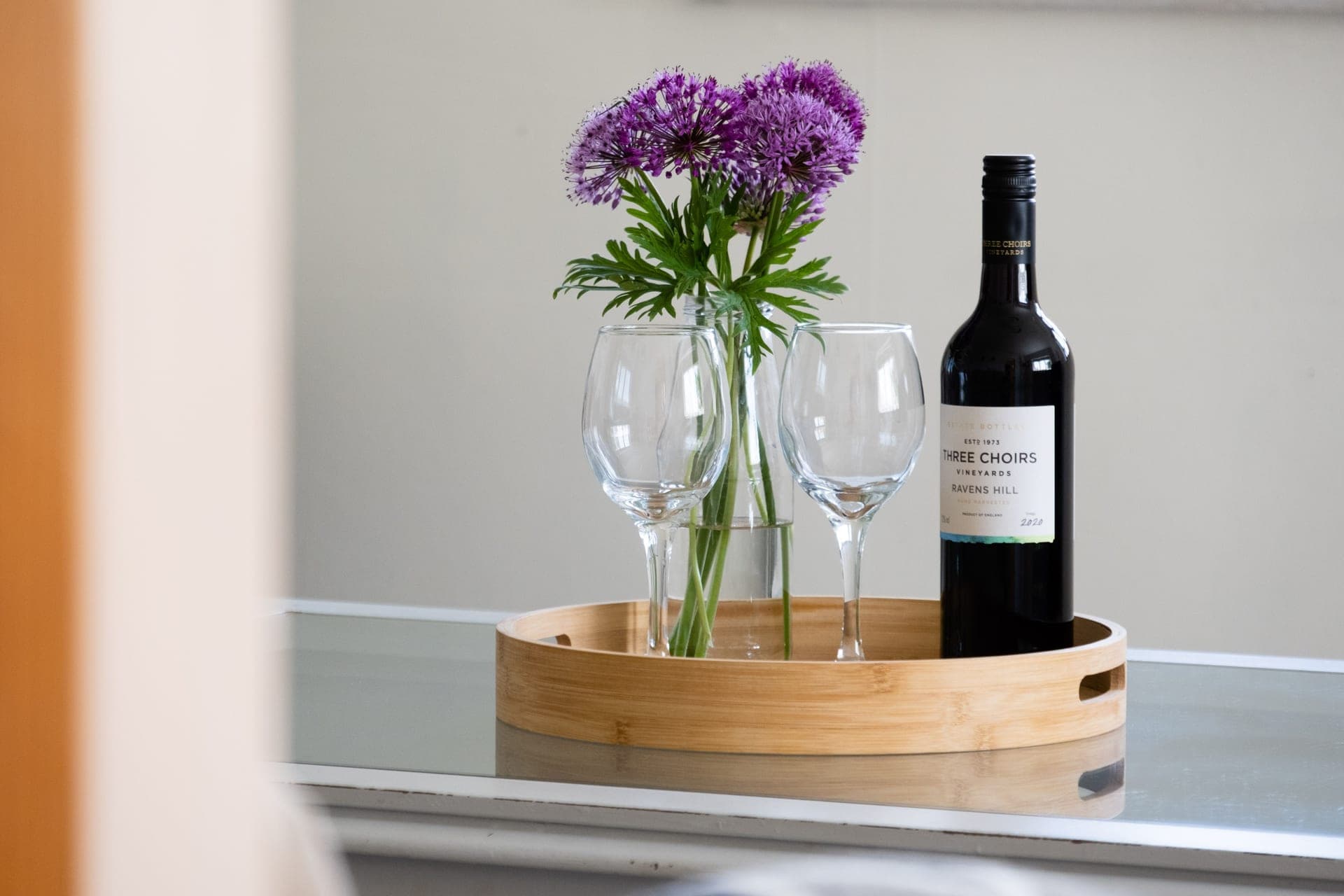 A wine bottle, glasses and flowers arranged on a wooden serving tray