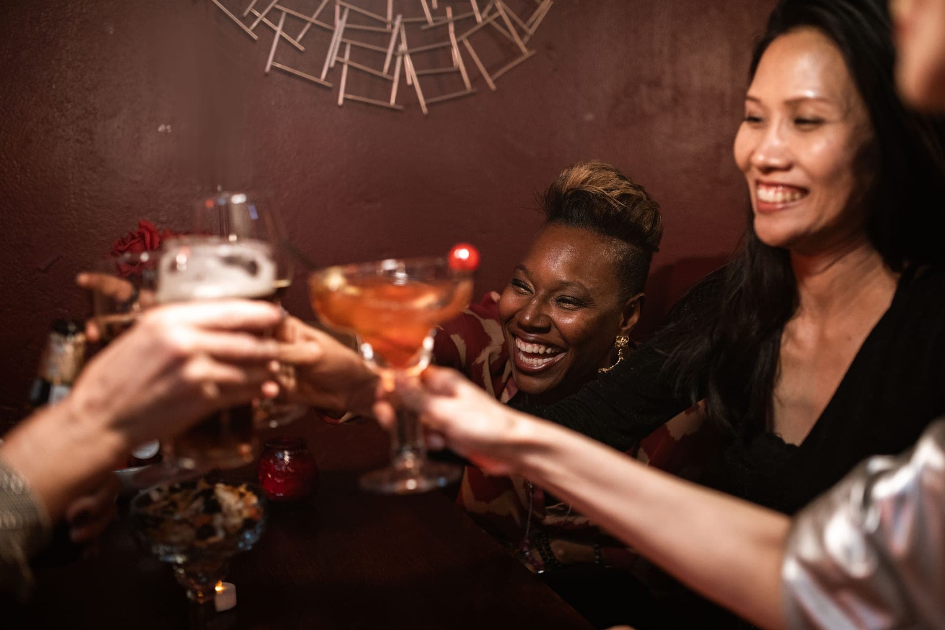 A group of friends raising drinks together in a warmly lit indoor bar setting