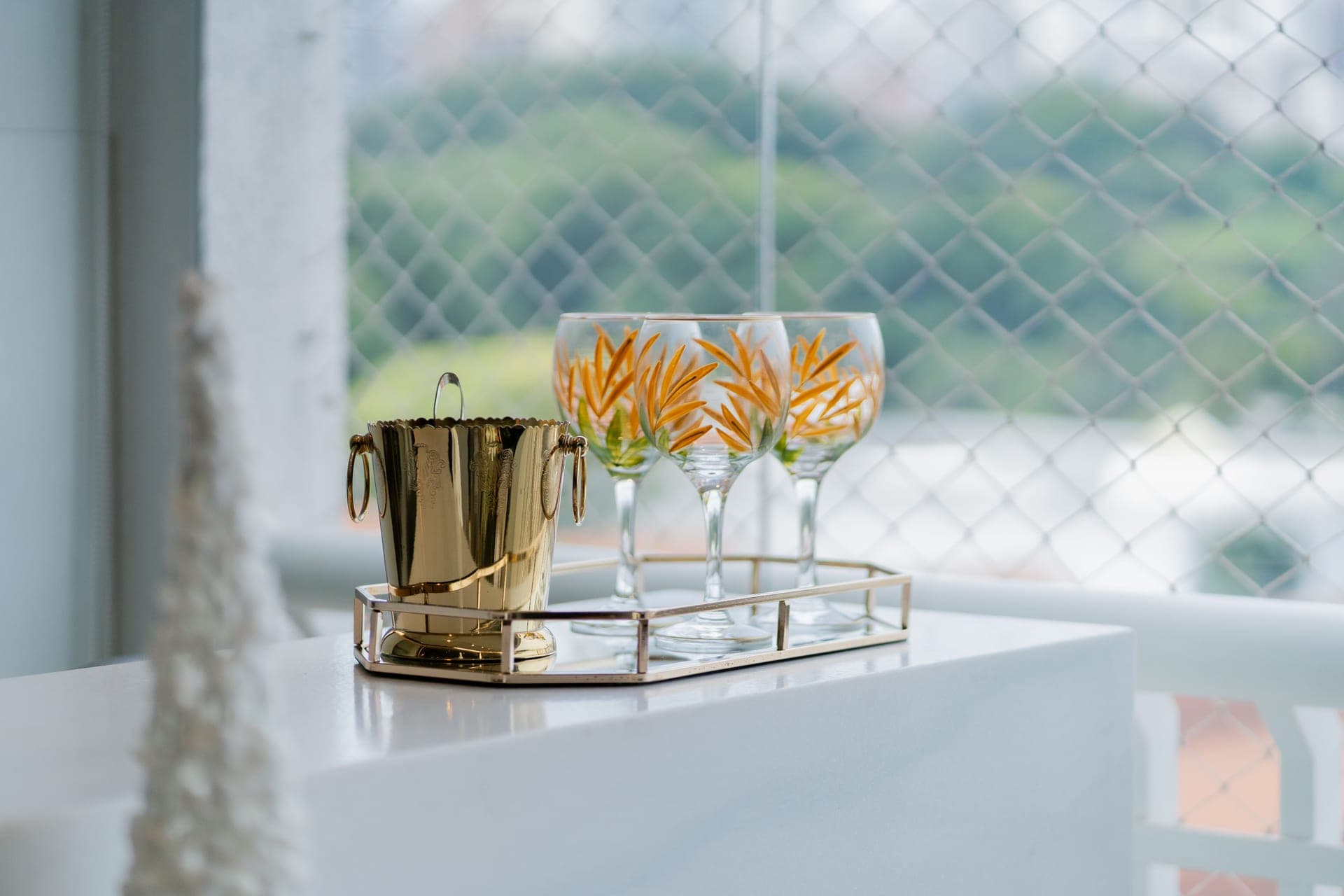 Stemmed glassware and a gold ice bucket arranged on a balcony table