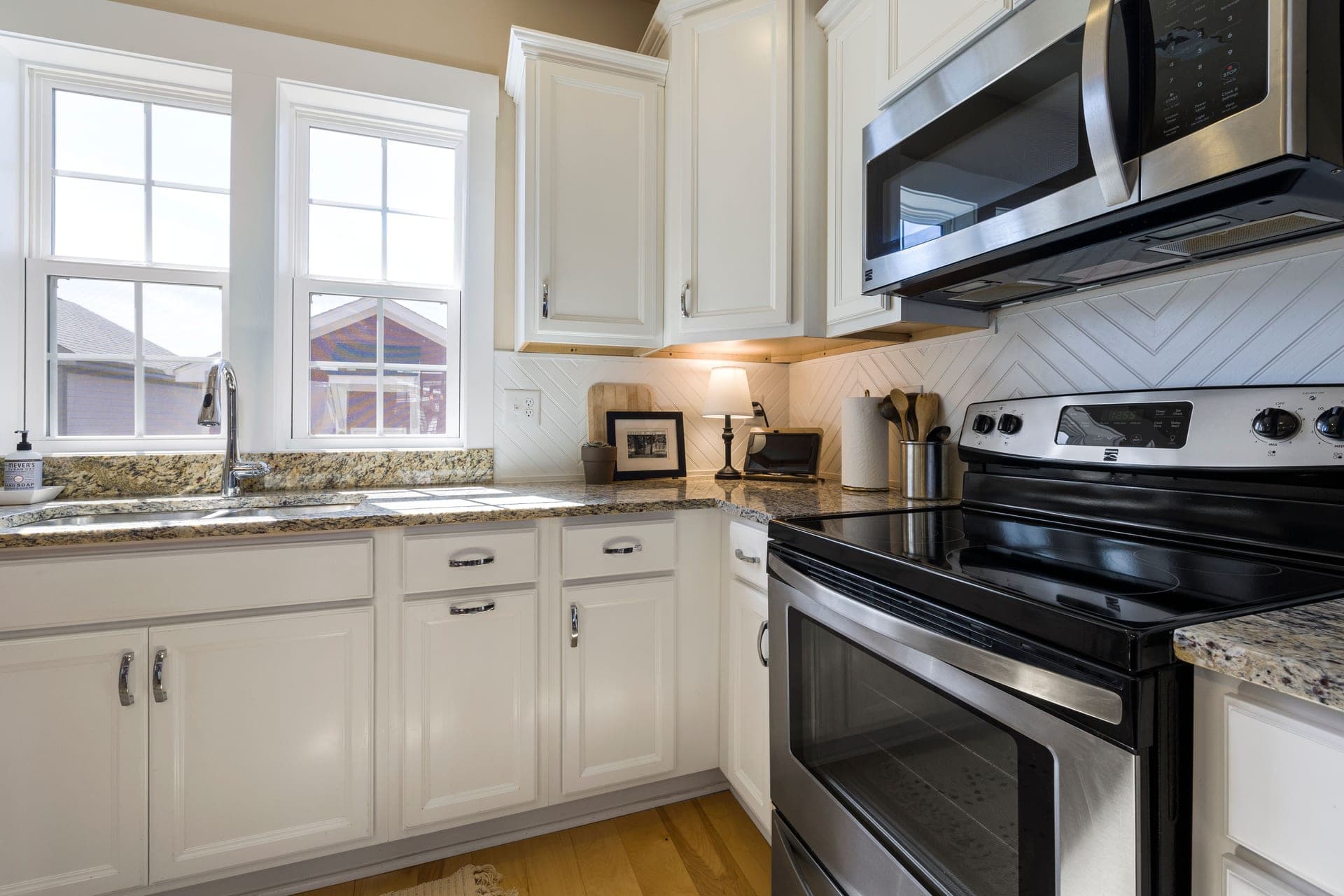 A bright modern kitchen with white cabinets and a stainless countertop microwave