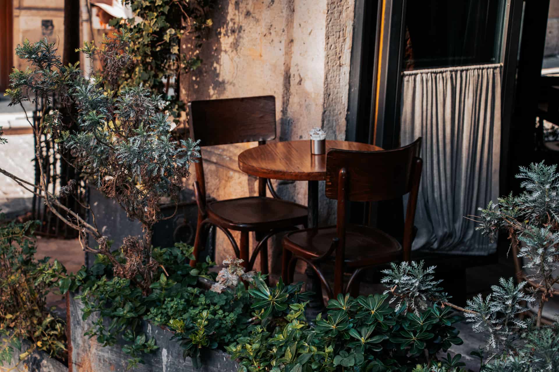 A wooden café table and chairs set out among greenery