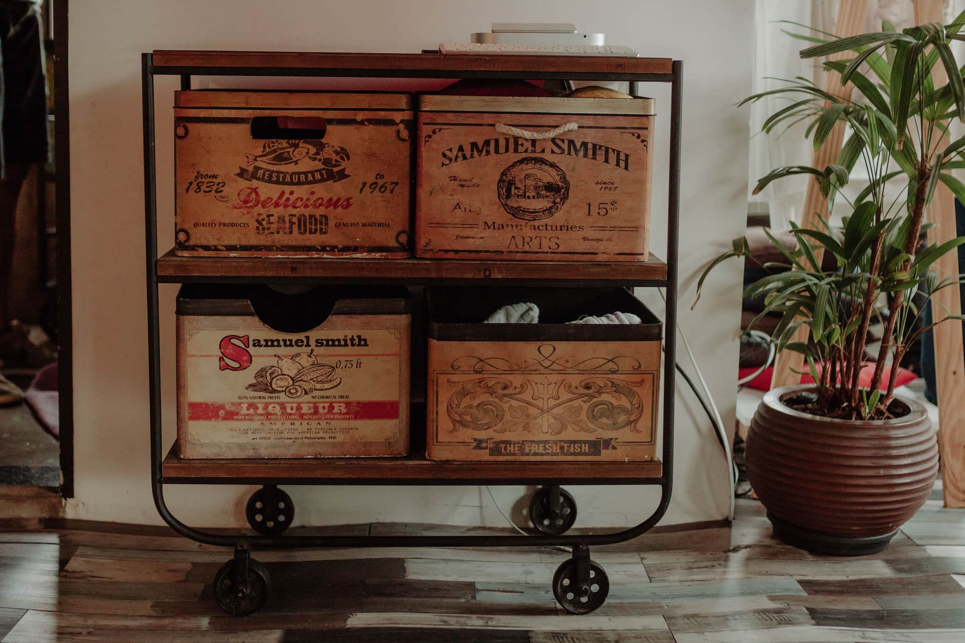 A metal-framed cart holding stacked wooden crates beside a potted plant indoors