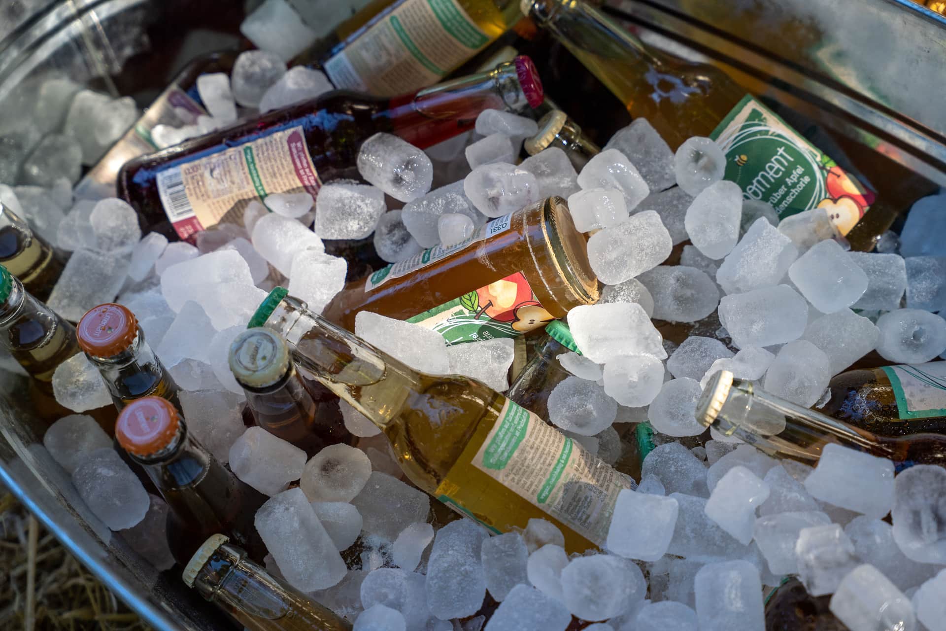 Bottles of cider and soda chilling on ice in a metal tub outdoors