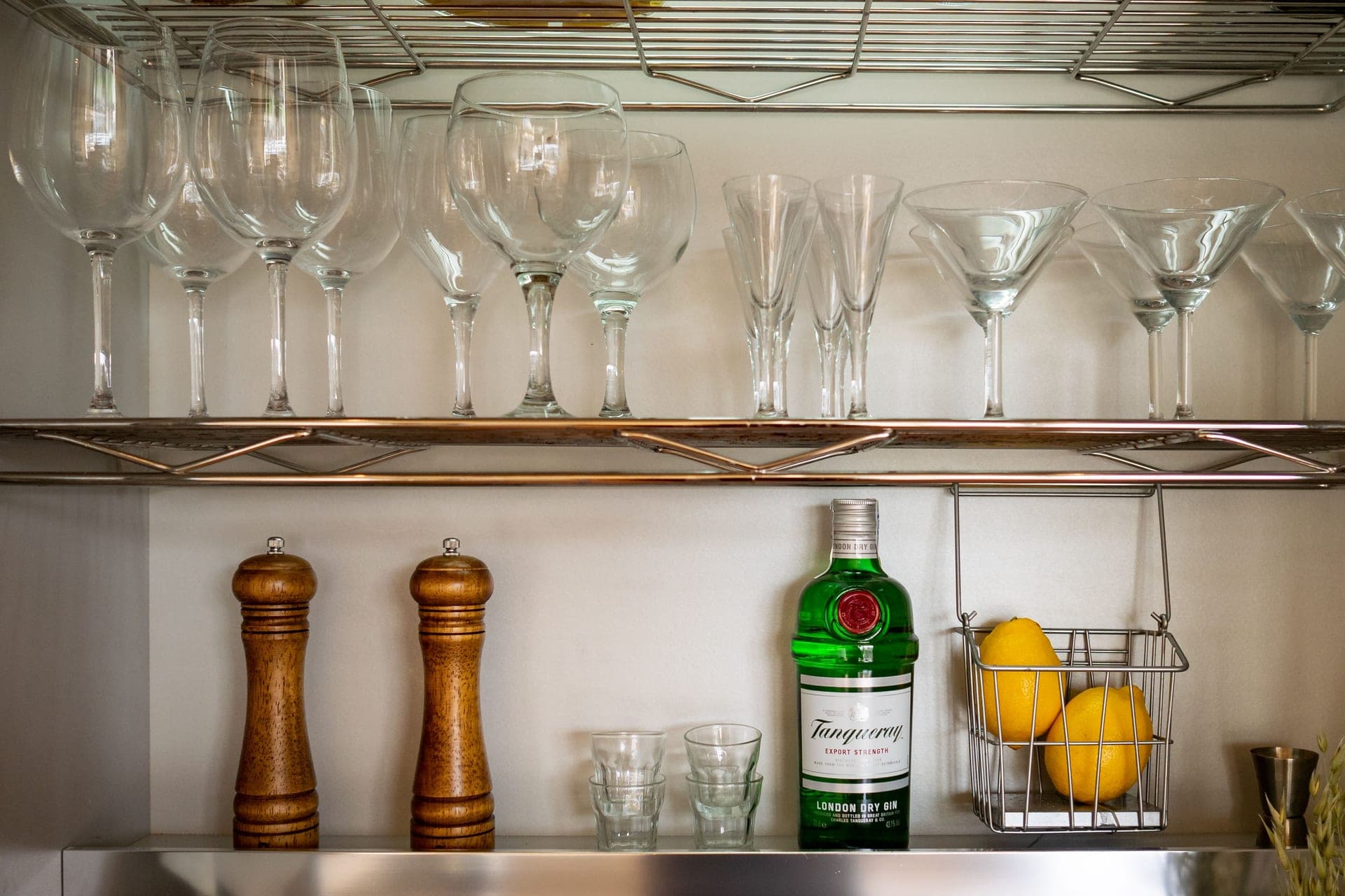 Wine and martini glasses on a metal shelf above a gin bottle and lemons