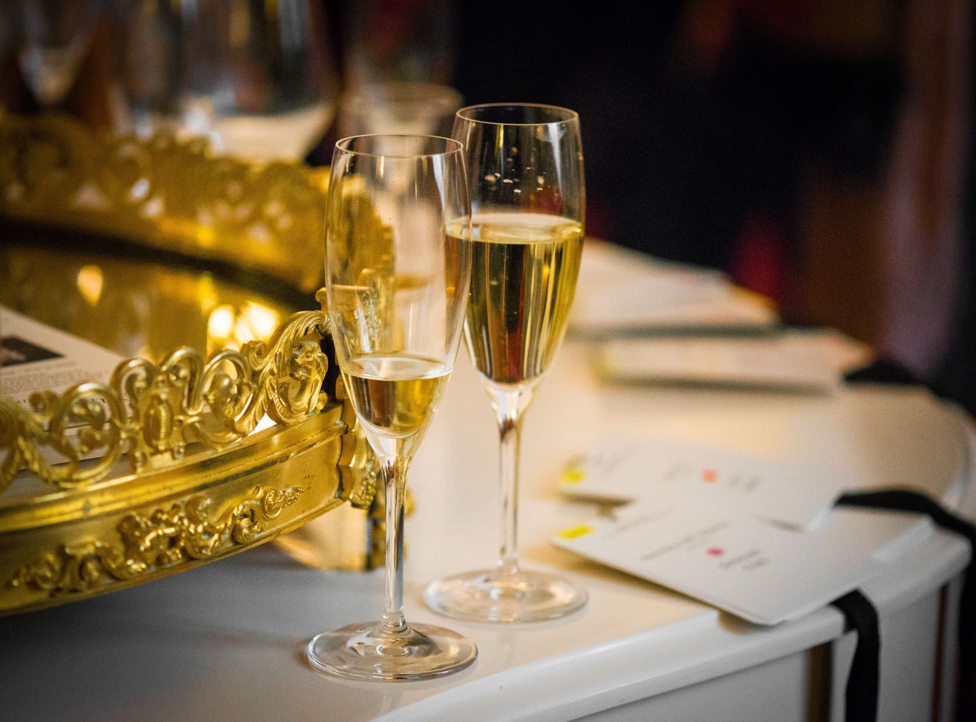 Two champagne flutes beside an ornate gilded tray on a white table