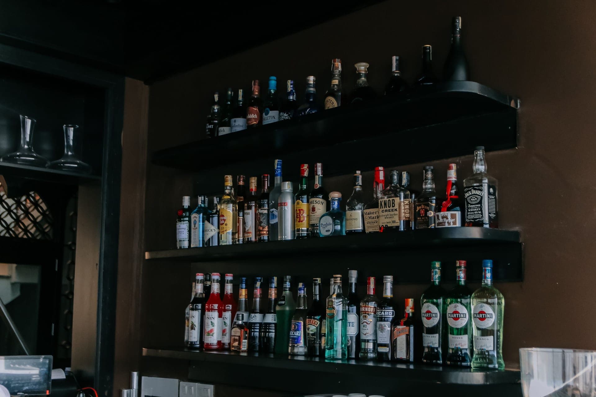 Three shelves of spirit bottles on a dark bar wall