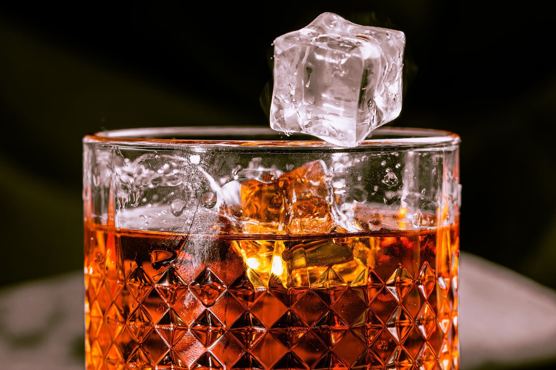 Whisky in a patterned glass with an ice cube dropping in