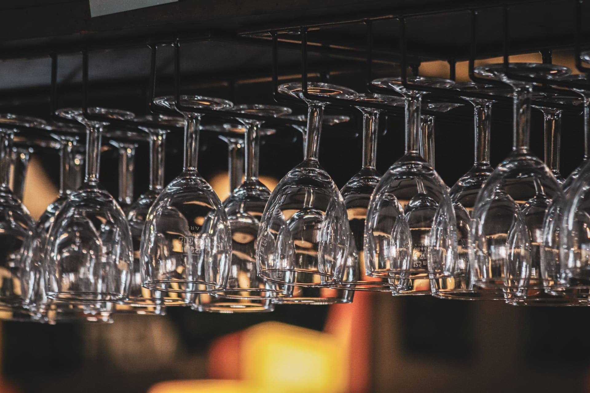 Upside-down wine glasses hanging on a rack in a softly lit bar